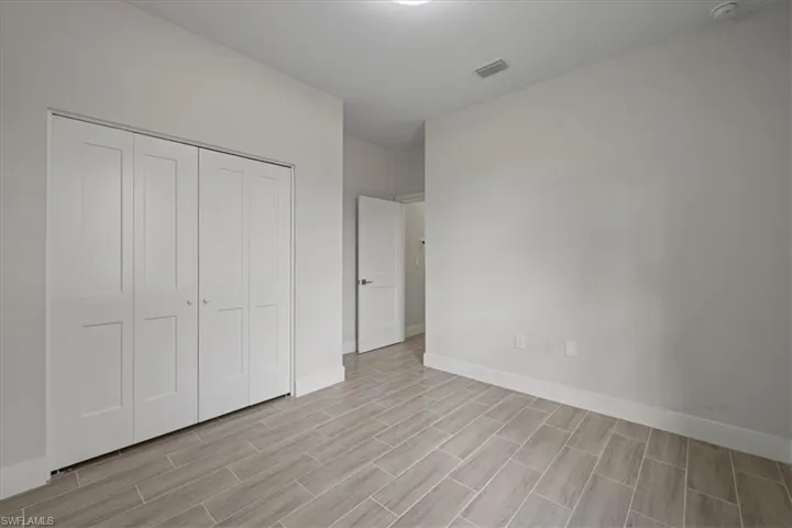 Interior room featuring neutral wall finishes, wood-finish tile flooring, a multi-panel interior door, and a built-in closet with folding doors