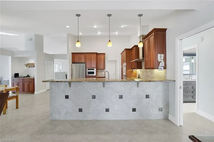 Kitchen with light stone countertops, a peninsula, freestanding refrigerator, hanging light fixtures, and tasteful backsplash