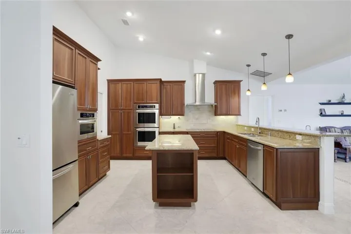 Kitchen featuring a peninsula, lofted ceiling, light stone counters, stainless steel appliances, and pendant lighting