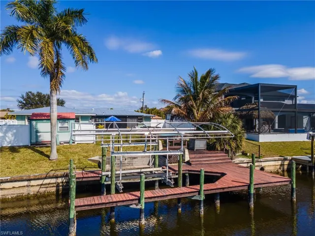 Dock area with boat lift, a water view, a yard, and glass enclosure