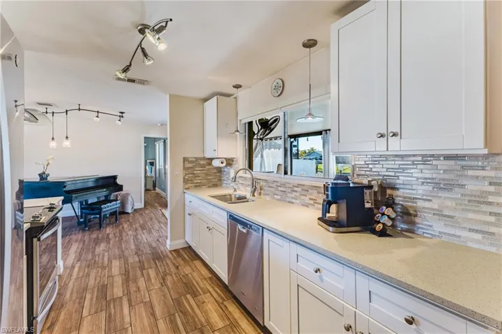 Kitchen featuring white cabinets, stainless steel appliances, wood tiled floors, light stone countertops, and track lighting
