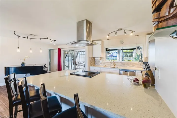 Kitchen featuring a kitchen breakfast bar, island exhaust hood, decorative backsplash, a peninsula, and light stone countertops