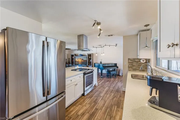 Kitchen featuring stainless steel appliances, island exhaust hood, white cabinetry, hanging light fixtures, and wood tiled floors