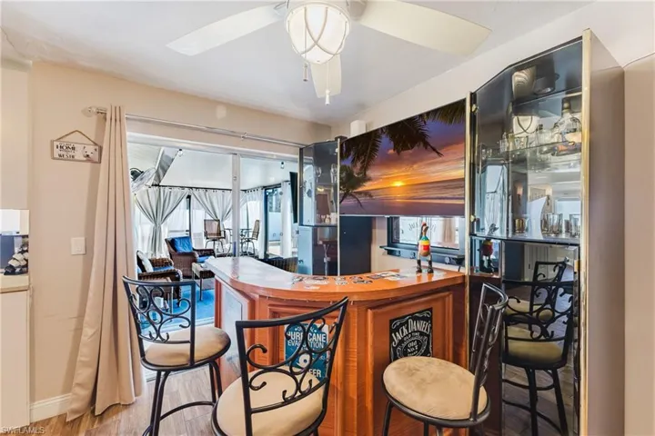 Indoor bar featuring light wood-style flooring, ceiling fan, and a sunroom