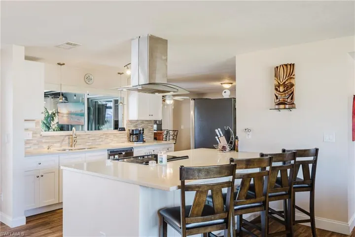 Kitchen with white cabinets, island exhaust hood, dark wood finished floors, stainless steel appliances, and a kitchen bar