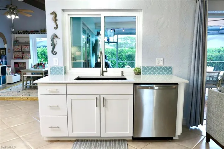 Kitchen with stainless steel dishwasher, white cabinets, light tile patterned floors, and sink