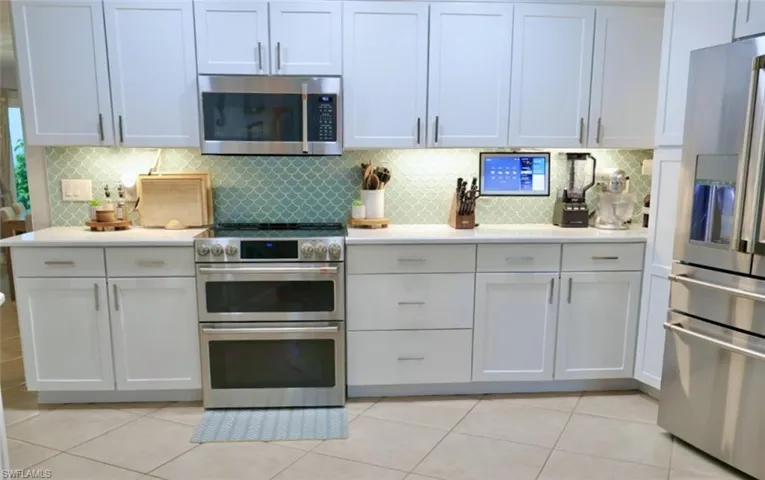 Kitchen with white cabinets, backsplash, light tile patterned floors, and stainless steel appliances