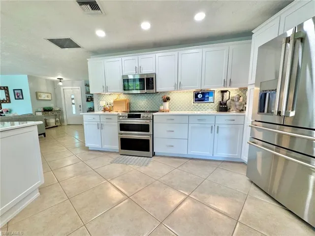 Kitchen with white cabinets, appliances with stainless steel finishes, backsplash, and light tile patterned flooring