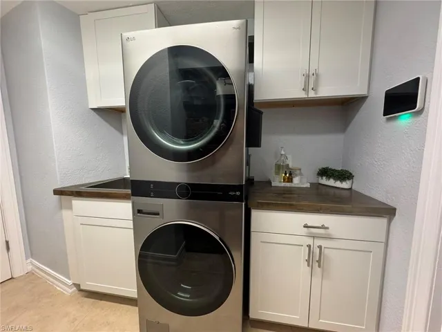 Laundry room featuring cabinets, light tile patterned floors, and stacked washer and clothes dryer