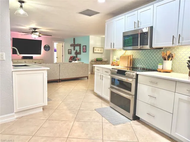 Kitchen featuring white cabinets, appliances with stainless steel finishes, backsplash, and light tile patterned flooring
