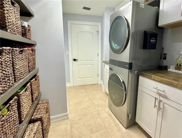 Washroom with cabinets, light tile patterned floors, and stacked washer and clothes dryer