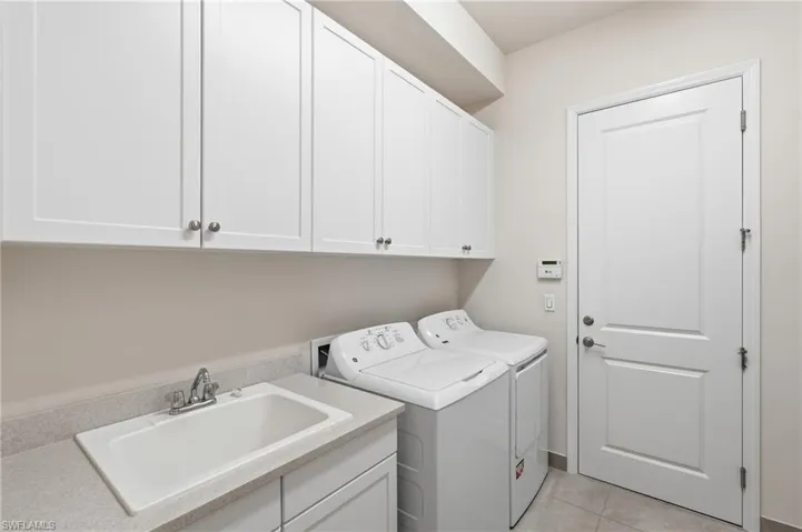 Laundry room featuring white shaker cabinetry, an integrated utility sink, a light-toned countertop, and light-colored floor tiling