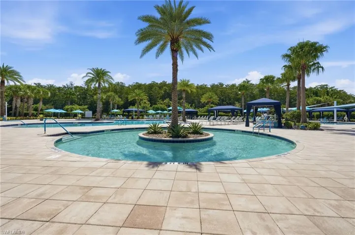 Resistance pool with an island palm tree, surrounding tiled patio, additional pools and multiple shaded cabanas.