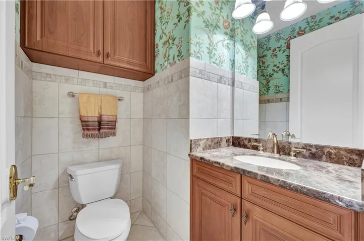 Half bath with vanity, wallpapered walls, tile walls, and wainscoting