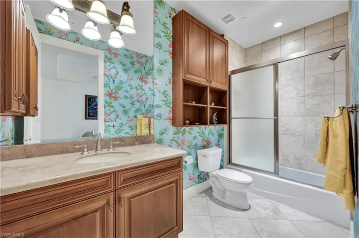Full bathroom featuring wallpapered walls, vanity, combined bath / shower with glass door, and light tile patterned floors