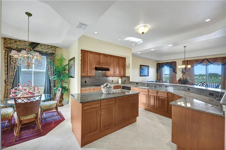 Kitchen featuring a chandelier, decorative light fixtures, dark stone countertops, brown cabinetry, and a kitchen island