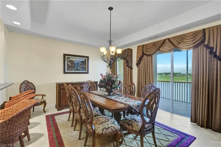Dining space with a chandelier, a tray ceiling, a water view, light tile patterned flooring, and recessed lighting