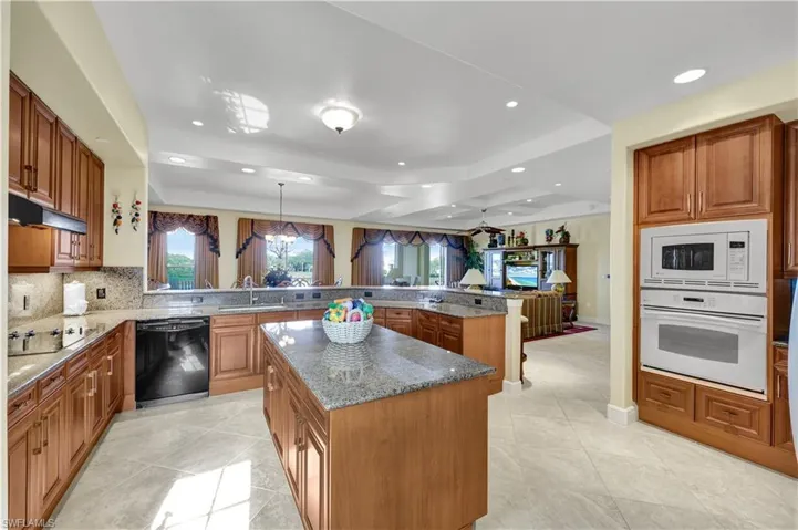 Kitchen with brown cabinets, black appliances, light stone countertops, a peninsula, and recessed lighting