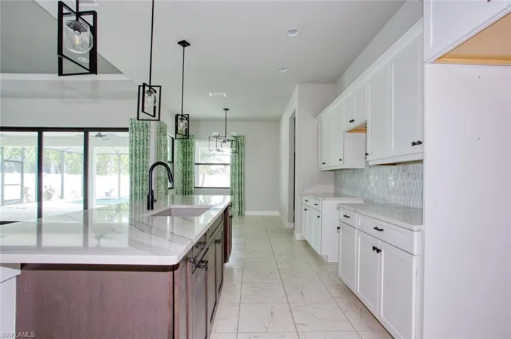 Open-concept kitchen featuring a large island with an undermount sink and matte black faucet, white shaker cabinetry with dark hardware, a light-toned tile backsplash, and recessed lighting