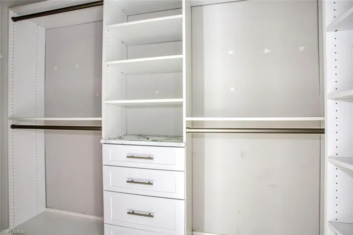 Built-in closet system featuring white shelving, multiple hanging rods, three drawers with bronze hardware, and a stone-finish countertop