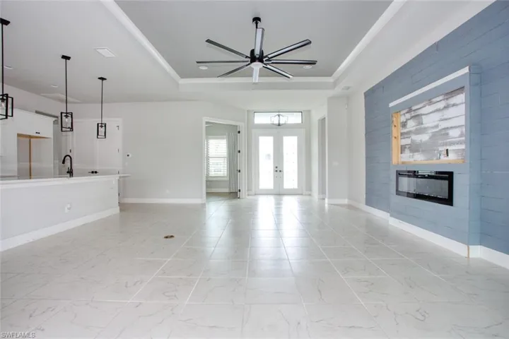 Spacious interior featuring large format floor tiling, a tray ceiling with a modern ceiling fan, and a contemporary linear fireplace