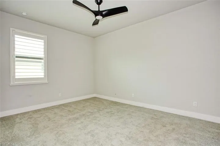 Carpeted room featuring a ceiling fan with black blades, a window with white louvered shutters, recessed lighting, and white baseboards