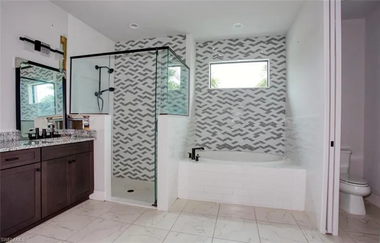 Contemporary bathroom featuring a walk-in shower with black-framed glass enclosure, an integrated soaking tub, a dual vanity with a granite countertop, patterned tile accents, and large format floor tiling