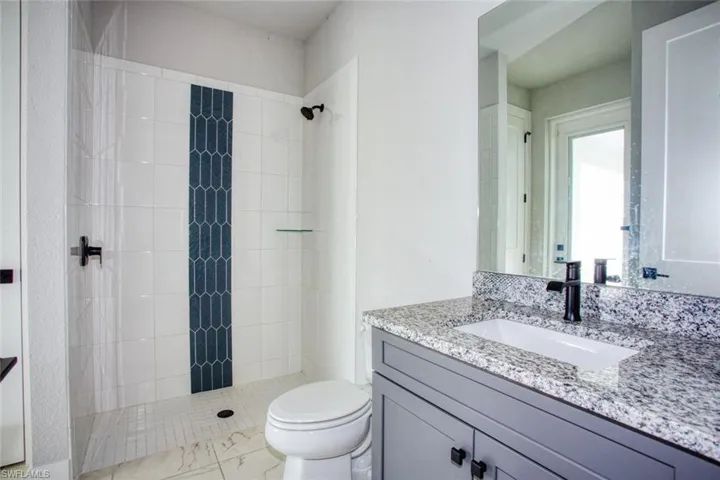 Bathroom featuring a walk-in shower with white subway tile and a dark blue picket tile accent, black shower fixtures, a white toilet, and a vanity with a light gray cabinet, a granite countertop, and a rectangular undermount sink with a black faucet