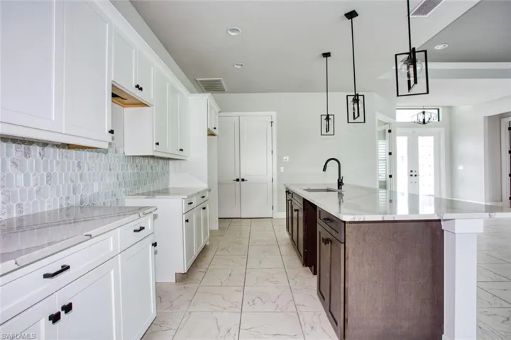 Spacious kitchen featuring an expansive center island, white shaker cabinetry, light-toned countertops, a mosaic tile backsplash, and large format tile flooring