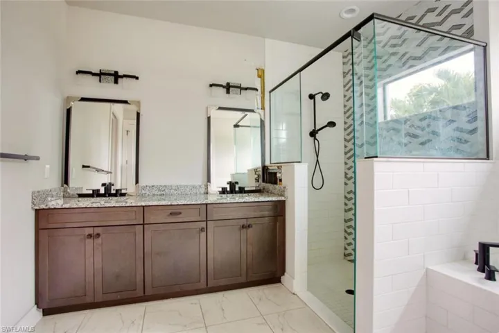 Bathroom featuring a dual vanity with granite-finish countertops, dark wood-finish cabinetry, and framed mirrors