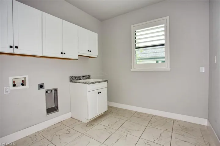 Utility space featuring overhead white cabinetry, a white base cabinet with a speckled countertop, a louvered window, and light-toned tile flooring