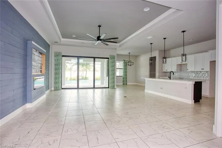 Spacious open-concept living area featuring large format tile flooring, a tray ceiling with a ceiling fan, a shiplap accent wall with a built-in media niche, and sliding glass doors opening to the exterior
