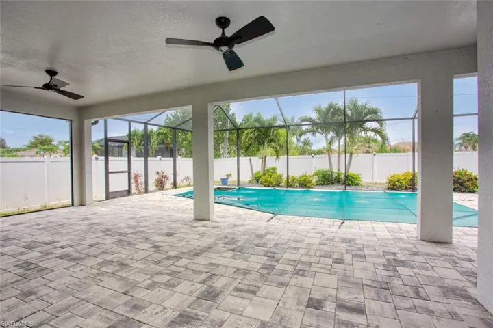 Spacious screened lanai featuring gray paver flooring, two ceiling fans, and a clear view of the enclosed swimming pool area