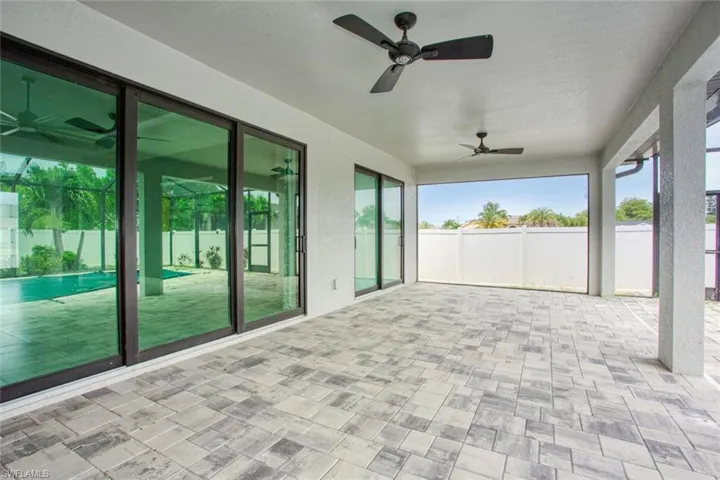 Expansive covered patio featuring patterned paver flooring, multiple ceiling fans, and a white privacy fence