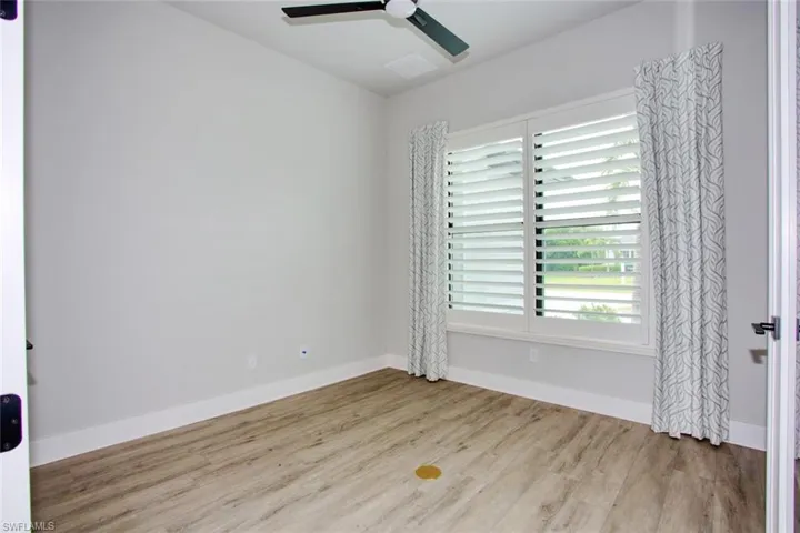 Room featuring wood-finish flooring, a ceiling fan with integrated lighting, and a large window with plantation shutters