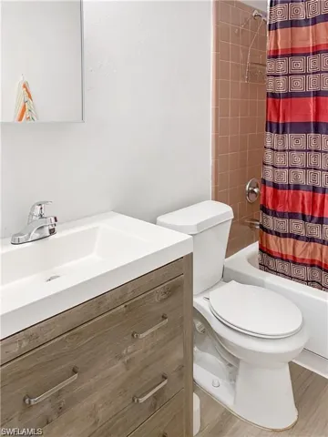 Full bathroom with wood-type flooring, toilet, vanity, and shower / tub combo with curtain