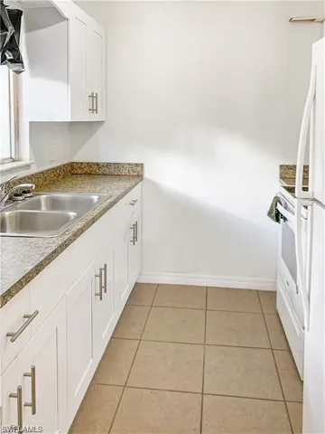 Kitchen with white cabinetry, white fridge, sink, and light tile patterned floors