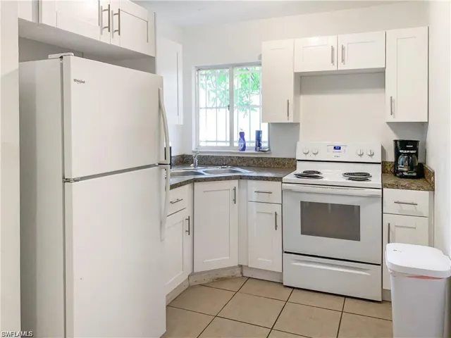 Kitchen with sink, white appliances, light tile patterned floors, and white cabinets