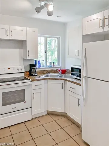 Kitchen featuring stone counters, white cabinets, white appliances, sink, and light tile patterned floors