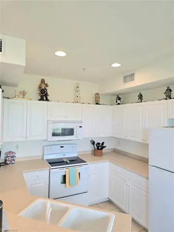 Kitchen with white appliances, white cabinetry, light countertops, and recessed lighting