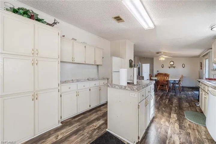 Kitchen featuring dark wood-style flooring, a textured ceiling, ceiling fan, white cabinetry, and a kitchen island