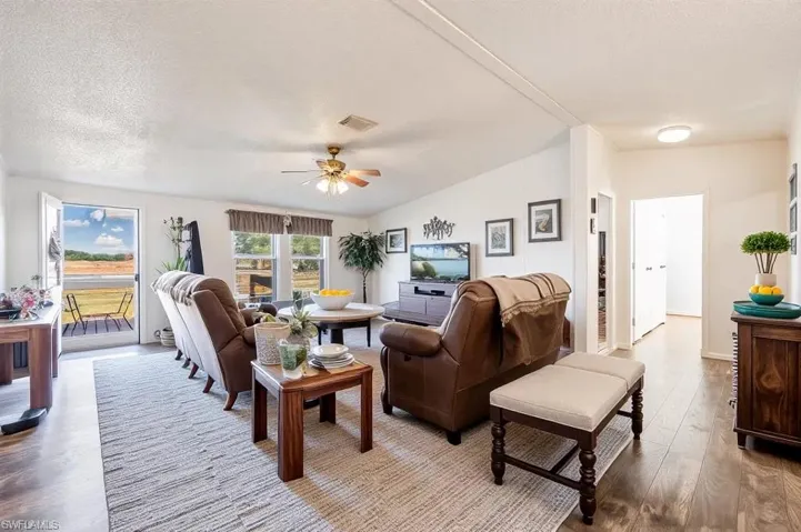 Living room with wood finished floors, a ceiling fan, lofted ceiling, and a textured ceiling