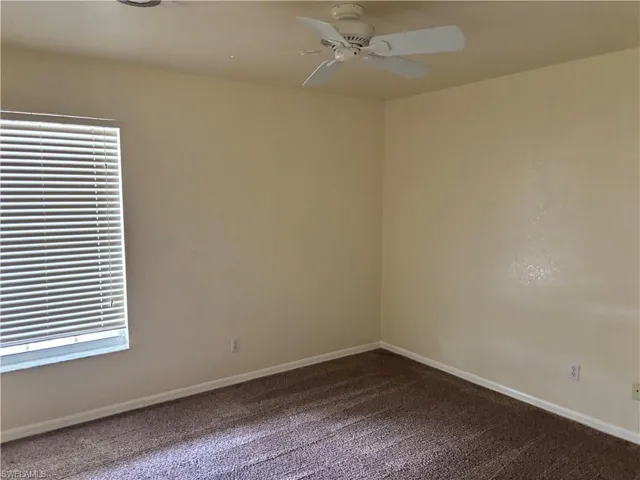 Unfurnished room featuring a ceiling fan and dark colored carpet