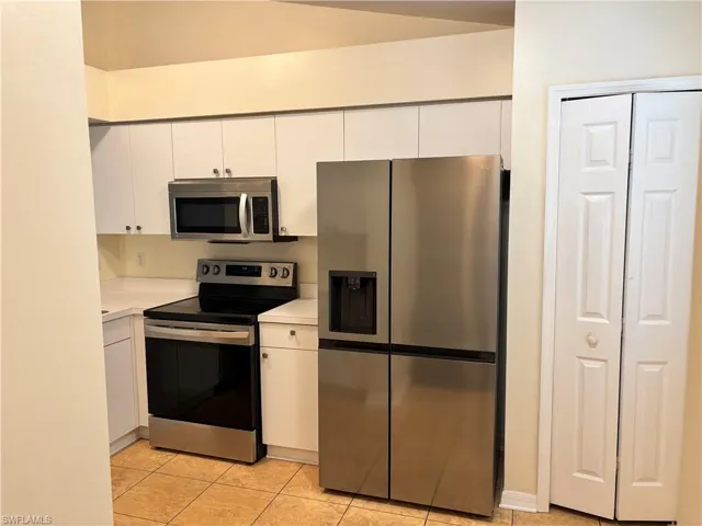Kitchen with stainless steel appliances, light countertops, white cabinetry, and light tile patterned flooring