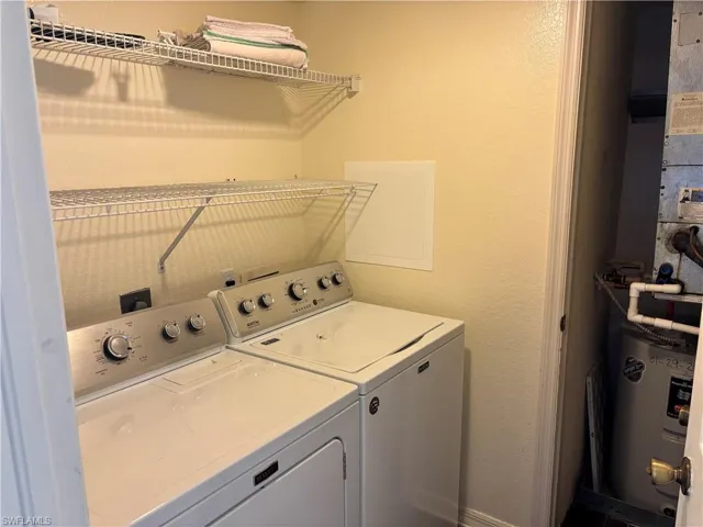 Laundry room with a textured wall, washer and clothes dryer, water heater, and heating unit