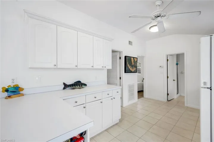 Kitchen with light countertops, white cabinetry, freestanding refrigerator, ceiling fan, and lofted ceiling