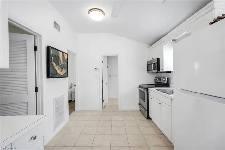 Kitchen featuring stainless steel appliances, lofted ceiling, white cabinets, light countertops, and light tile patterned flooring