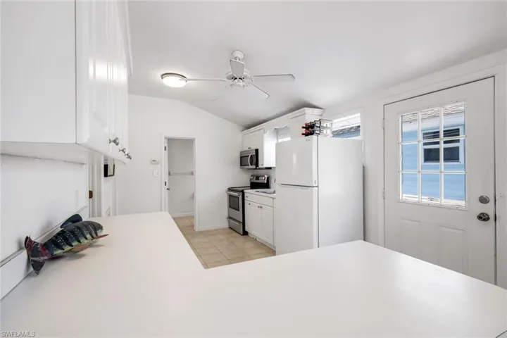 Kitchen with stainless steel appliances, light countertops, white cabinetry, and vaulted ceiling