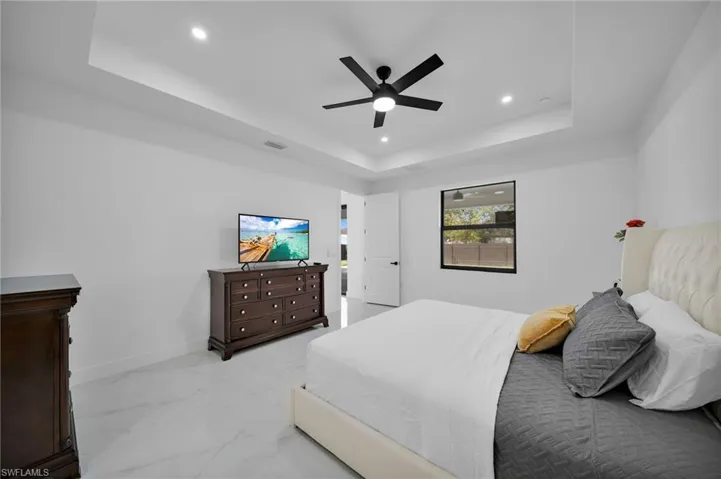 Bedroom with a raised ceiling, recessed lighting, light marble finish floors, ceiling fan, and baseboards