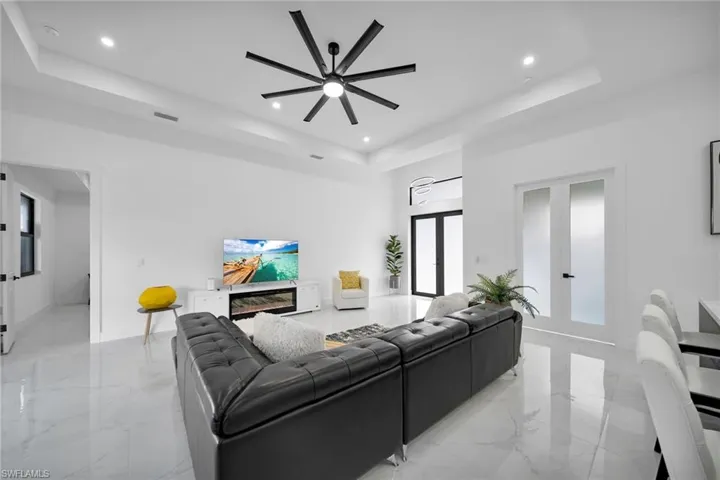 Living area featuring a raised ceiling, light marble finish floors, recessed lighting, a ceiling fan, and french doors